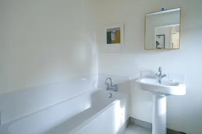 a white bathroom with a sink and a bath tub at Lowlands in Thorpeness