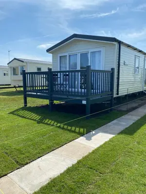 a mobile home with a large deck on the grass at Stylish 3 Bedroom caravan near the Beach in Walton-on-the-Naze