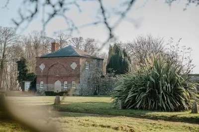an old brick house in a field with a tree at Butley Priory Cottage in Woodbridge