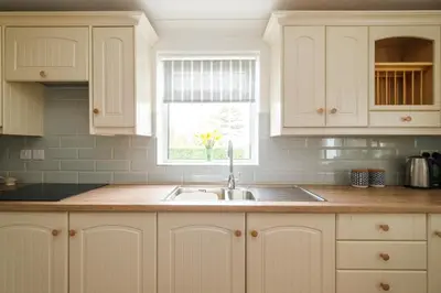 a kitchen with white cabinets and a sink and a window at The Lodge, Aldringham in Aldringham
