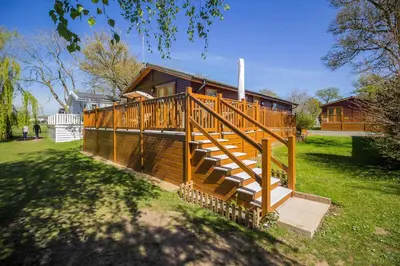 a large wooden house with a large deck at Stunning Lodge For Hire At Carlton Meres In Suffolk Ref 60013M in Saxmundham