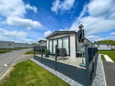 a tiny house with a porch and an umbrella at Modern Caravan With Large Decking Area, Ref 60057Ch in Saxmundham