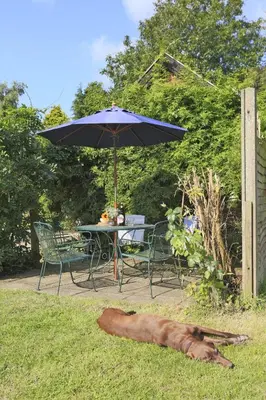 a dog laying in the grass next to a table and an umbrella at 3 Bed in Leiston oc-wil in Theberton