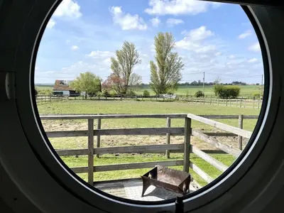 a round window looking out at a farm field at Armadilla 1 at Lee Wick Farm Cottages & Glamping in Clacton-on-Sea