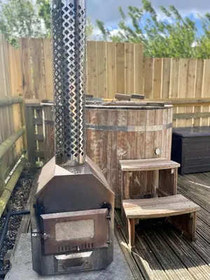 a grill with a wooden barrel and a wooden fence at Armadilla 1 at Lee Wick Farm Cottages & Glamping in Clacton-on-Sea